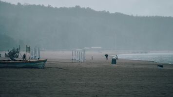 A deserted beach with strong winds and mist, closed umbrellas, and a wooden boat under overcast skies