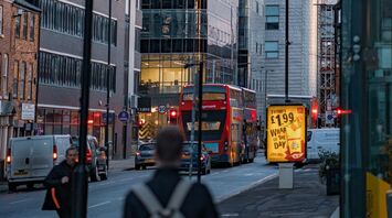 A busy urban street in Greater Manchester with modern buildings, a red double-decker bus, and illuminated signage
