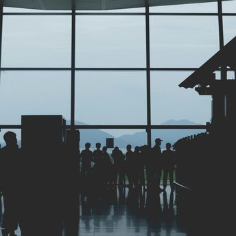 Silhouetted passengers queuing inside a Vietnamese airport terminal with a glass wall revealing scenic mountain views