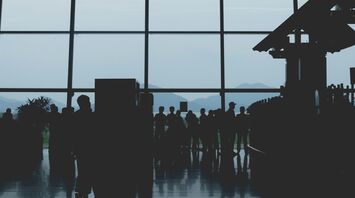 Silhouetted passengers queuing inside a Vietnamese airport terminal with a glass wall revealing scenic mountain views