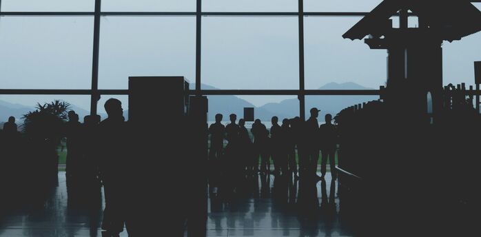 Silhouetted passengers queuing inside a Vietnamese airport terminal with a glass wall revealing scenic mountain views