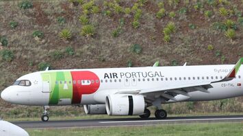TAP Air Portugal aircraft on a runway with a green hillside in the background