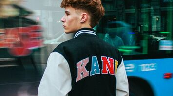 A young man standing on a city street in Madrid with a bus passing by in the background, showcasing urban transportation in Madrid