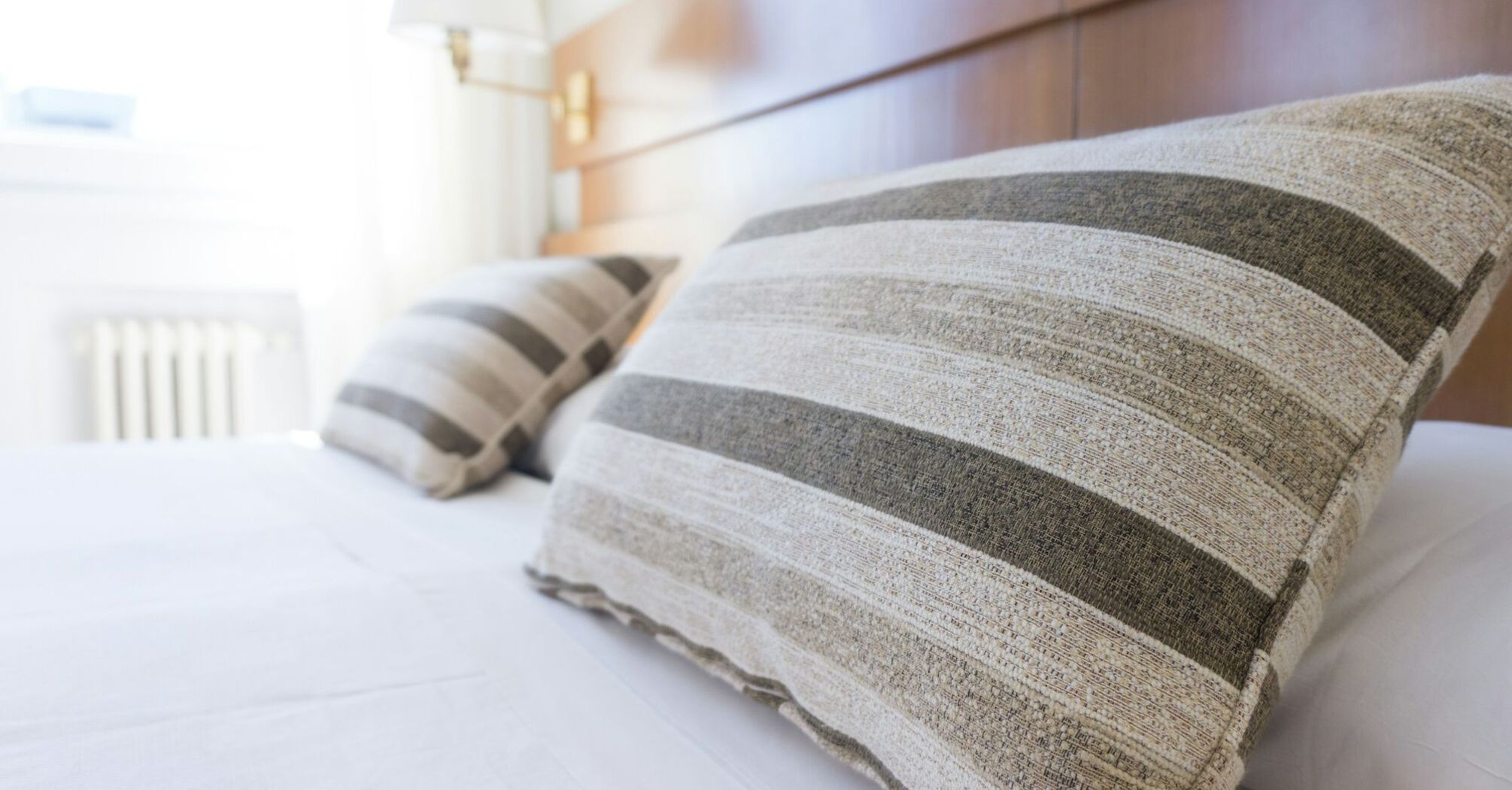 A neatly made hotel bed with striped pillows in a bright, modern room