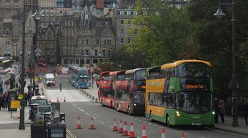 A busy street in Edinburgh featuring buses, historic buildings, and pedestrians