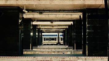 A deserted railway platform in Italy with a stationary train in the background, framed by concrete structures