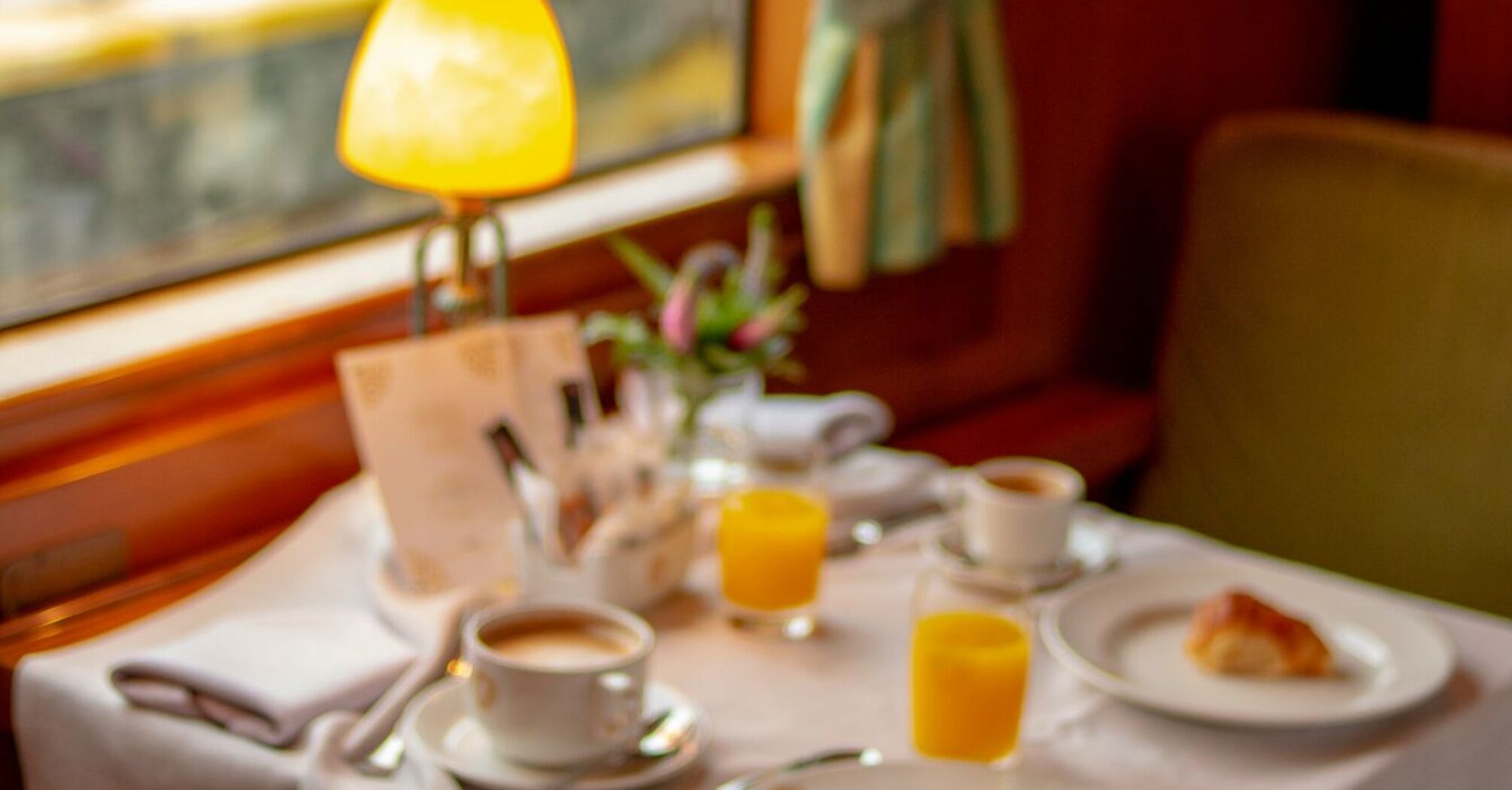 A dining table with breakfast setup inside a luxurious vintage train carriage, showcasing a scenic countryside view outside the window