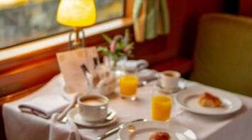 A dining table with breakfast setup inside a luxurious vintage train carriage, showcasing a scenic countryside view outside the window