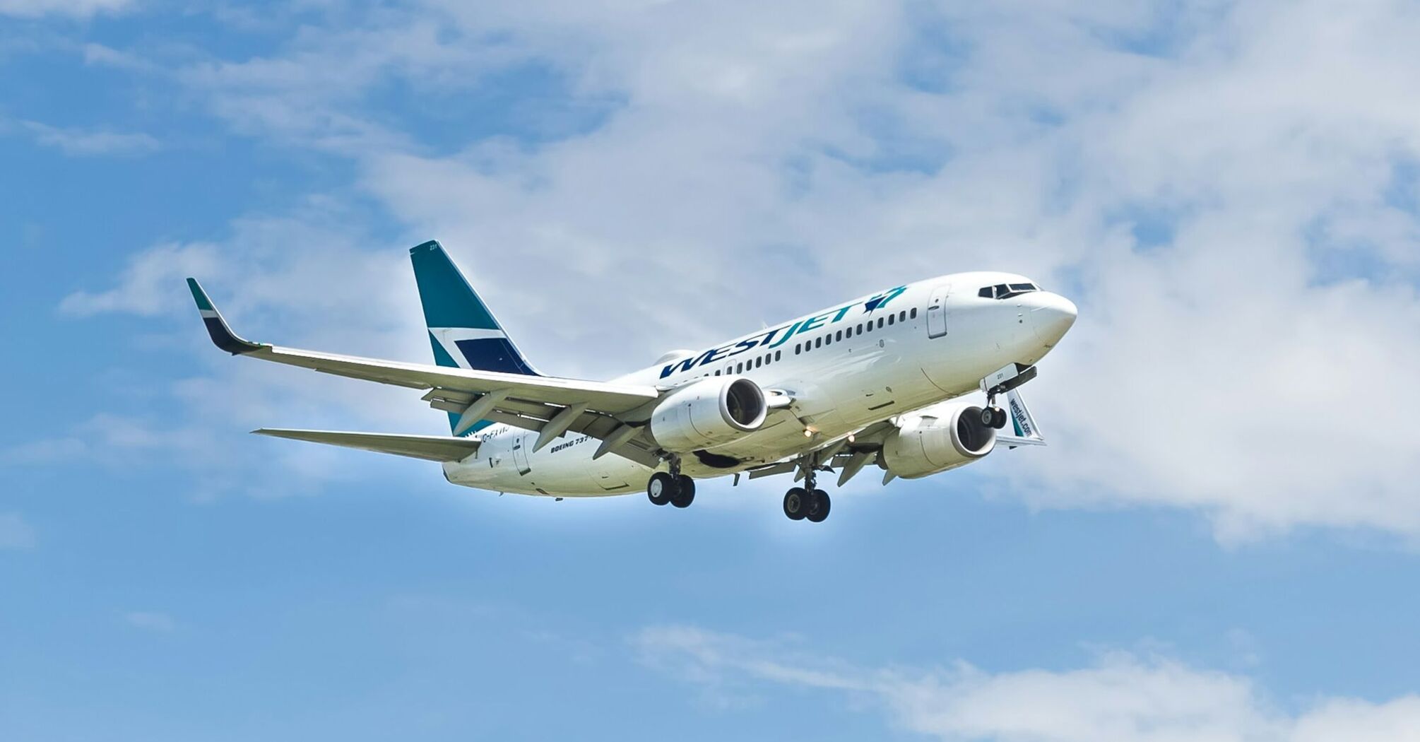 A WestJet airplane in flight under a blue sky, representing air travel