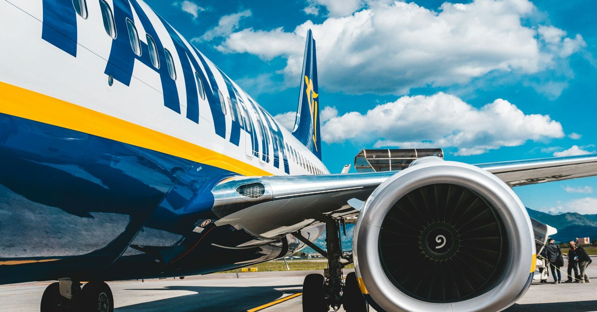 Close-up of a Ryanair aircraft engine and fuselage under a bright blue sky at an airport