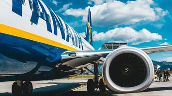 Close-up of a Ryanair aircraft engine and fuselage under a bright blue sky at an airport
