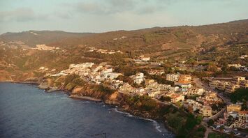 A coastal village in Sardinia with rolling hills and lush greenery, overlooking the Mediterranean Sea under soft evening light