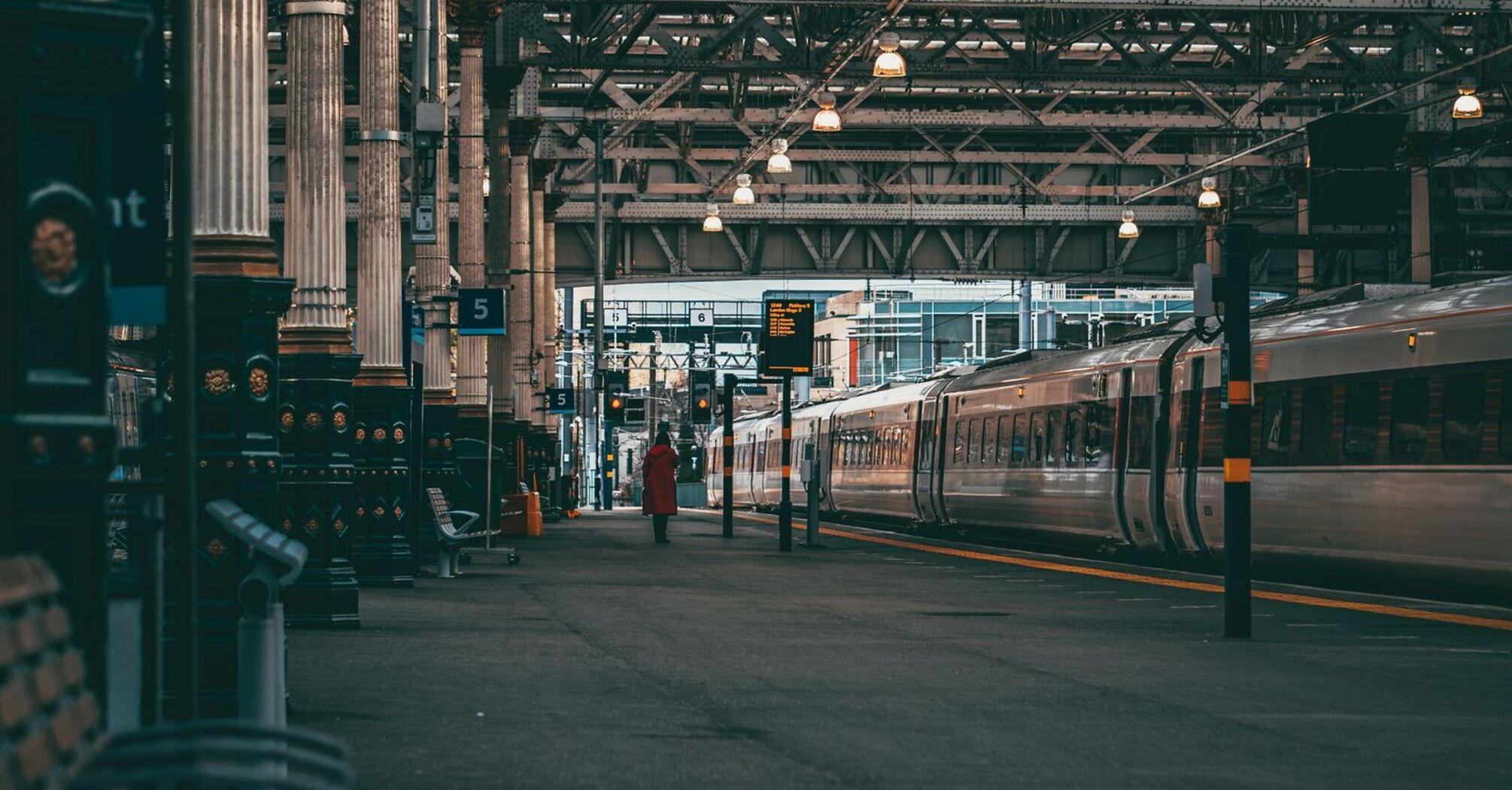 Interior view of a busy train station with modern trains, large iron beams, and dim lighting