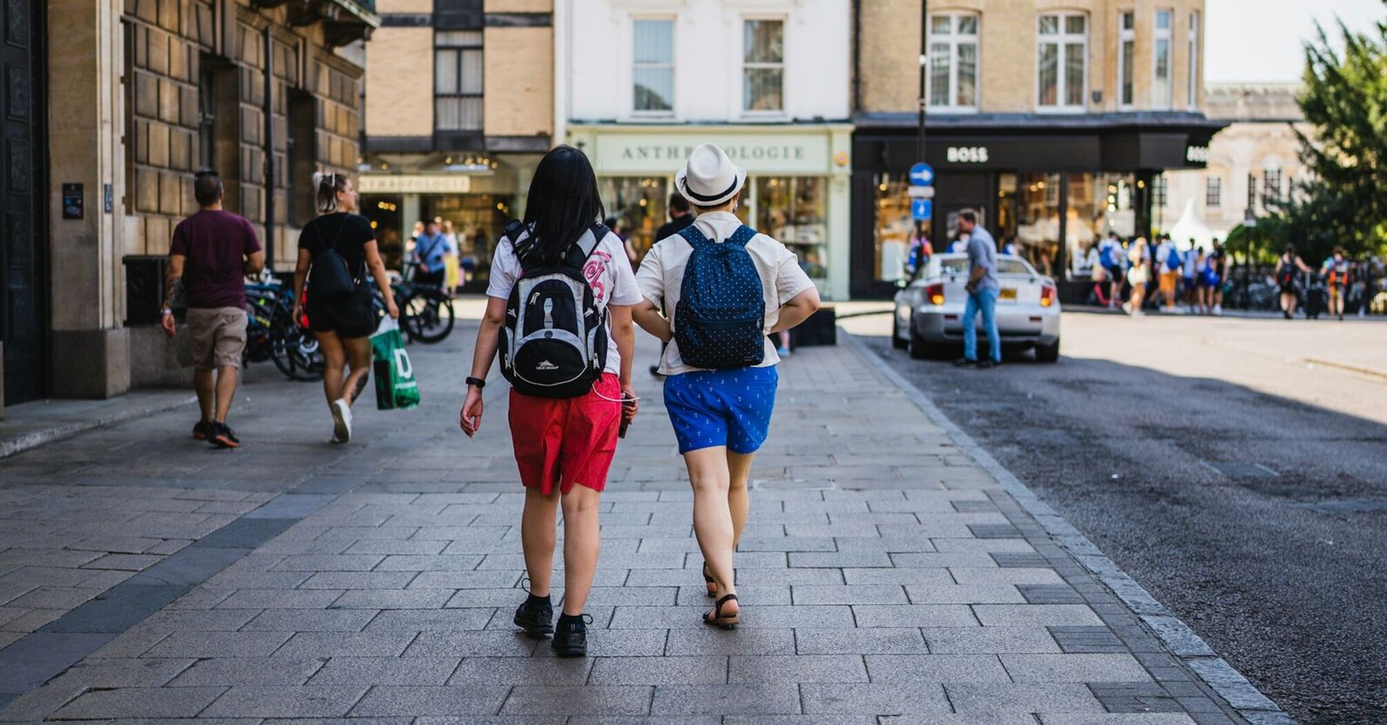 Two tourists walking down a city street, exploring an urban area with shops and historic buildings in the background