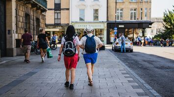 Two tourists walking down a city street, exploring an urban area with shops and historic buildings in the background