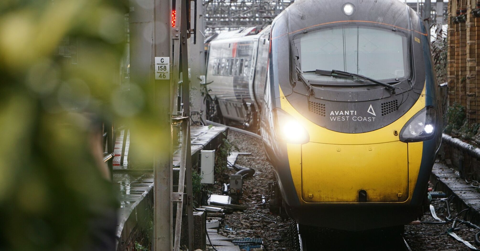 A yellow and black Avanti West Coast train at a station platform, surrounded by tracks and infrastructure