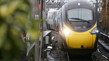 A yellow and black Avanti West Coast train at a station platform, surrounded by tracks and infrastructure