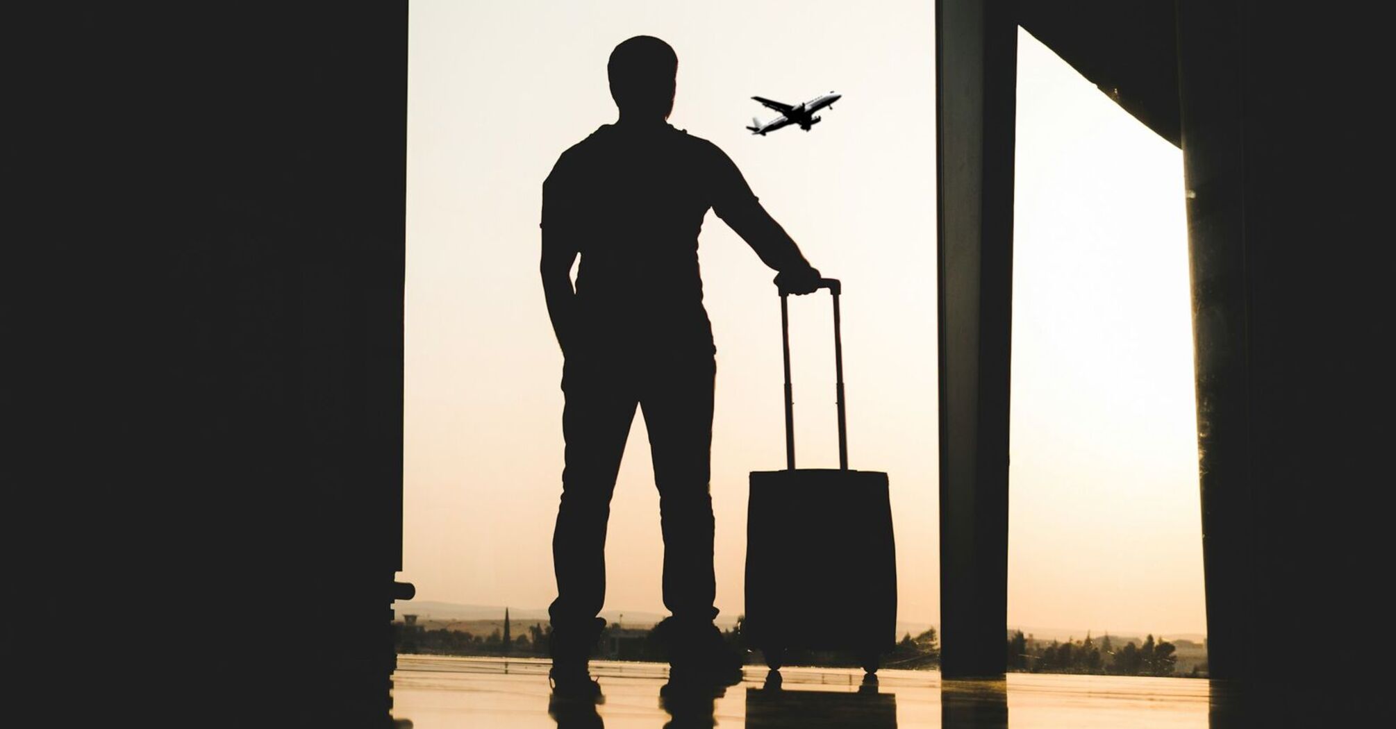 A silhouette of a traveler with a suitcase at an airport terminal, with a plane visible in the sky