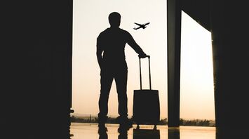 A silhouette of a traveler with a suitcase at an airport terminal, with a plane visible in the sky