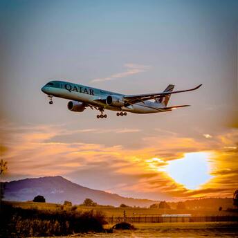 Qatar Airways plane landing against a vibrant sunset with a scenic rural backdrop