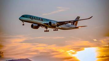Qatar Airways plane landing against a vibrant sunset with a scenic rural backdrop