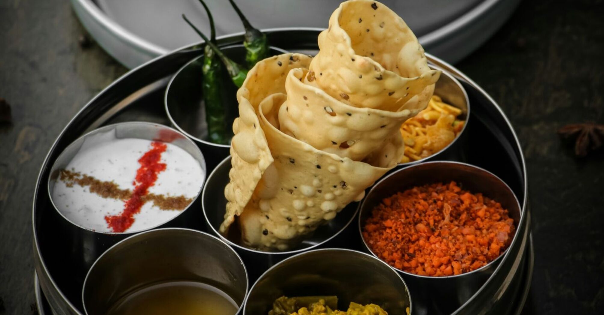 A traditional Indian meal served with papad, chutneys, and a pressure-cooked curry, showcasing vibrant and rich flavors