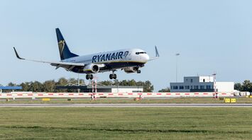 A Ryanair plane landing at an airport, with clear skies and a terminal building in the background
