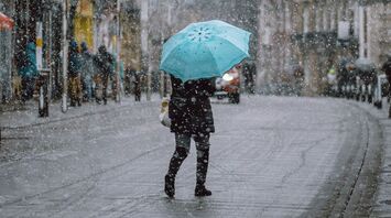 A person holding a turquoise umbrella walks through a snowy street in an urban area