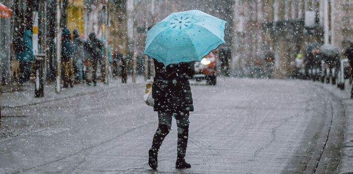A person holding a turquoise umbrella walks through a snowy street in an urban area
