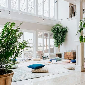 A serene wellness retreat space with large windows, lush indoor plants, cozy cushions, and natural light creating a tranquil atmosphere