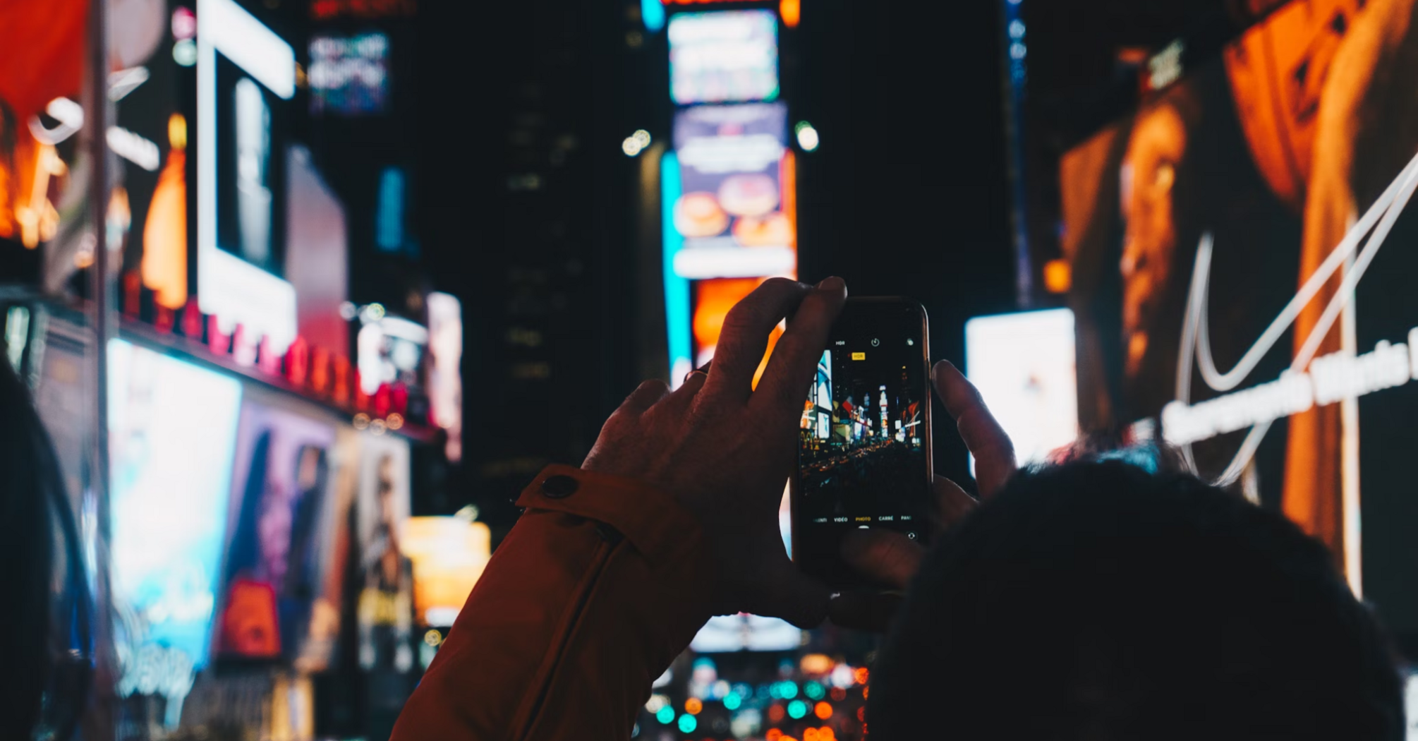 A person taking a photo of bright neon lights in Times Square at night