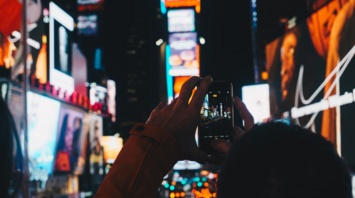 A person taking a photo of bright neon lights in Times Square at night