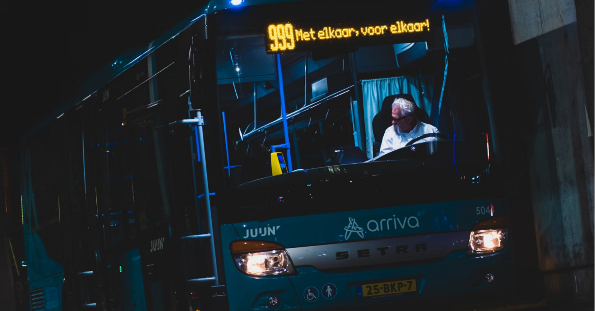 An Arriva bus parked at a station with a digital timetable displaying upcoming departures at night