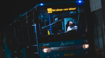 An Arriva bus parked at a station with a digital timetable displaying upcoming departures at night