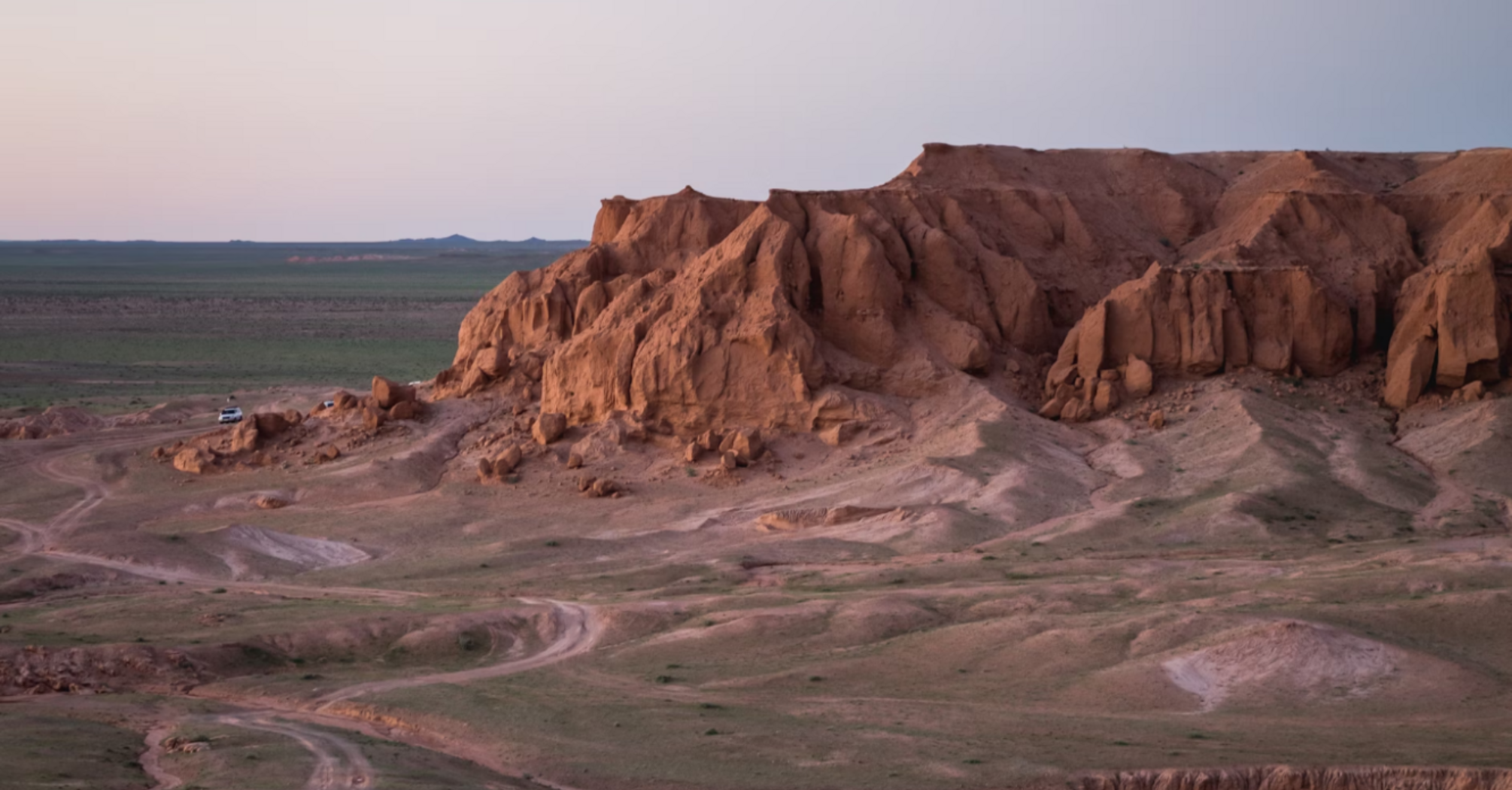 Scenic view of Mongolia's Gobi Desert at sunset, featuring rugged rock formations and vast open terrain