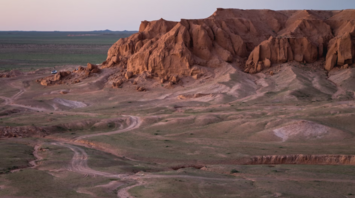 Scenic view of Mongolia's Gobi Desert at sunset, featuring rugged rock formations and vast open terrain