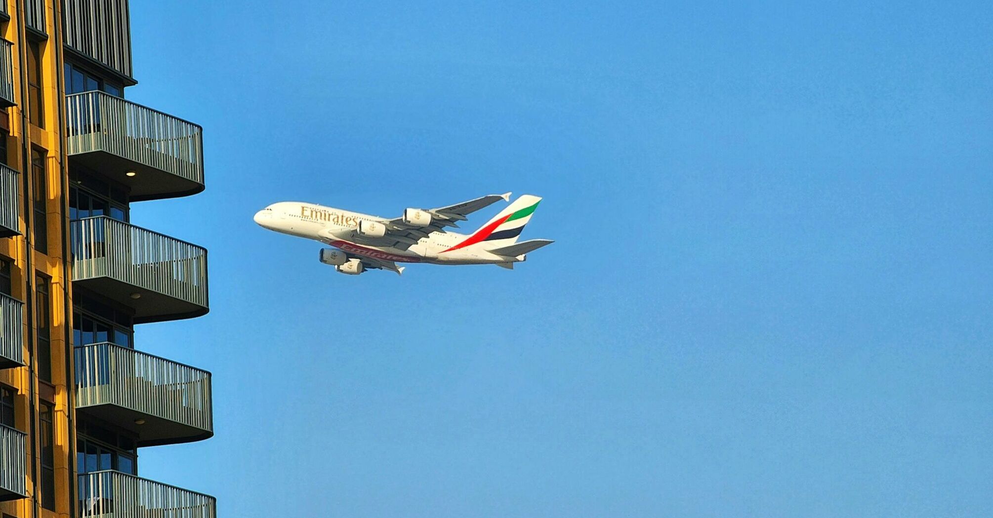 Emirates A380 flying near a residential building under a clear blue sky