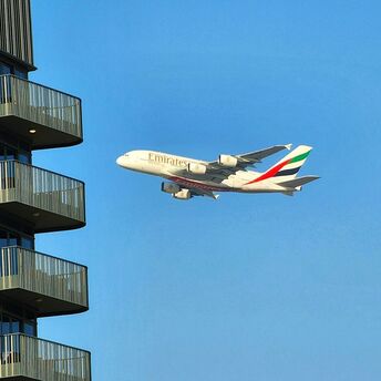 Emirates A380 flying near a residential building under a clear blue sky