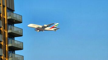 Emirates A380 flying near a residential building under a clear blue sky