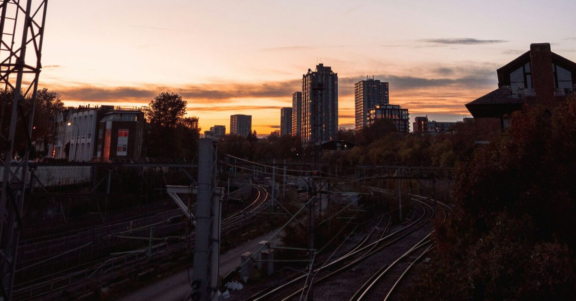 A railway track at sunset with a city skyline in the background, illustrating urban transport infrastructure