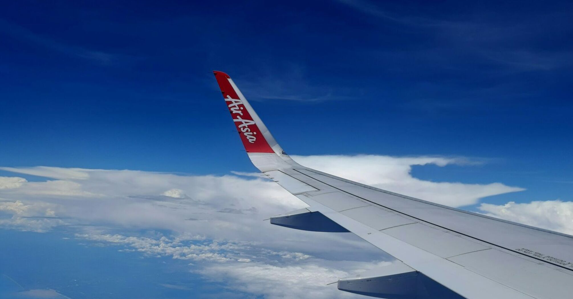 AirAsia wing view from a plane flying above a coastline under a blue sky