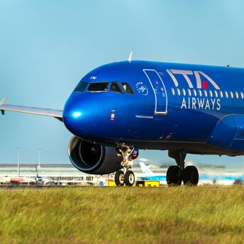A blue ITA Airways aircraft taxiing on the runway at an airport