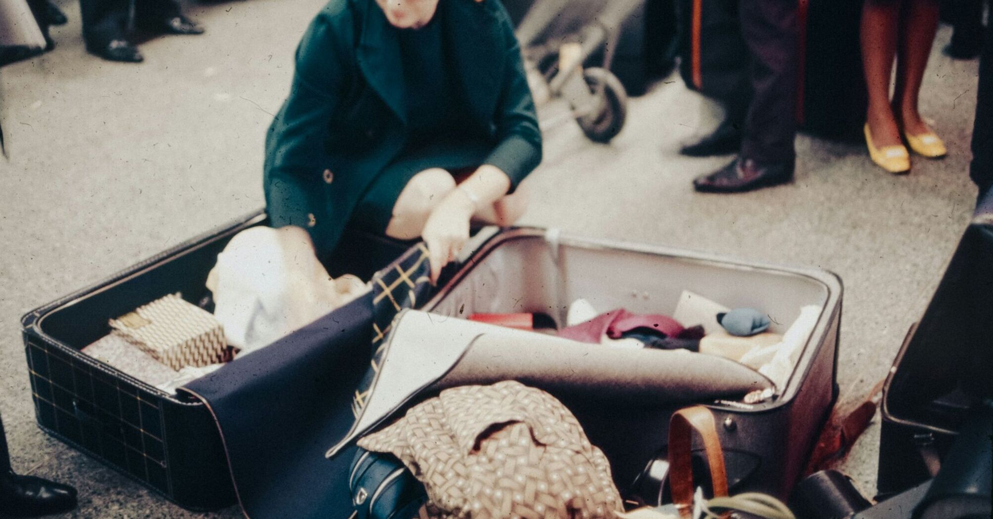 A traveler packing a suitcase outdoors, surrounded by luggage and other travelers