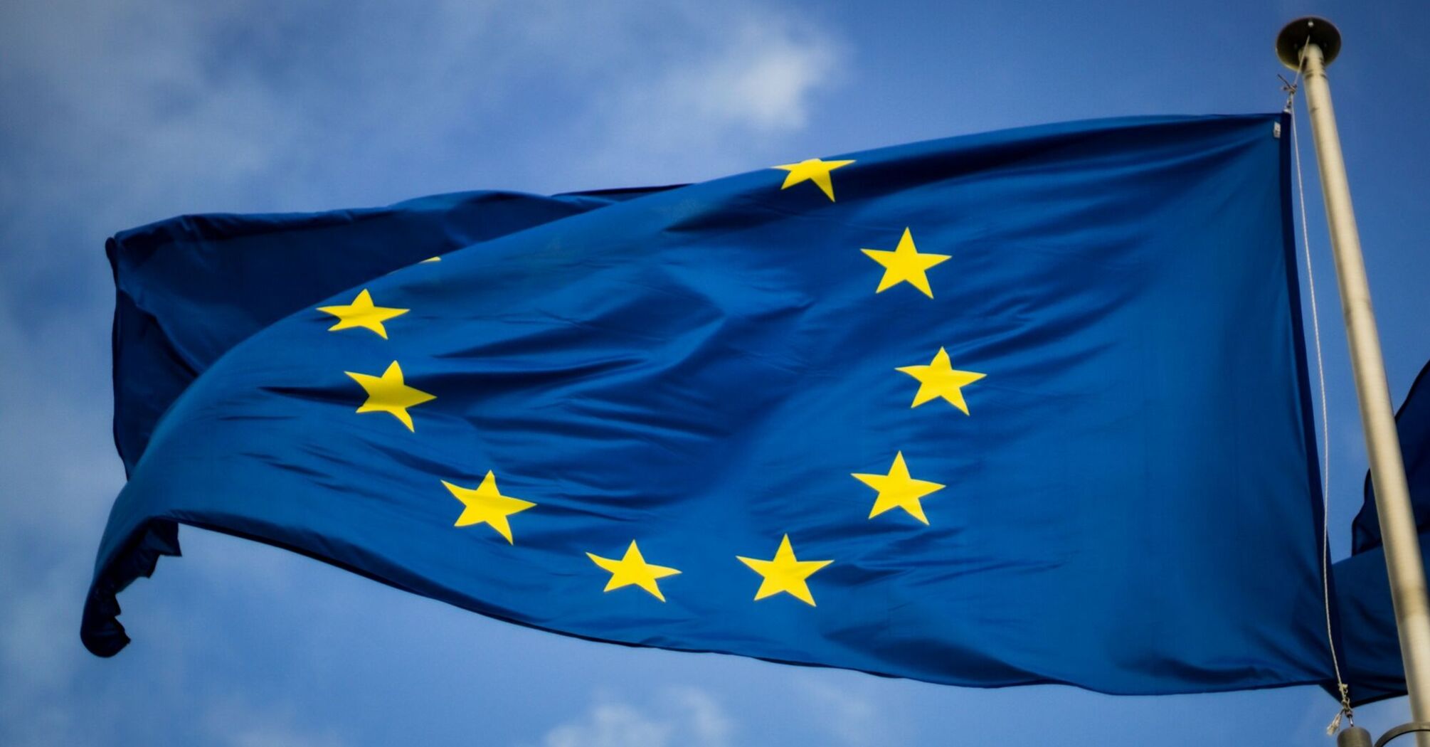 A close-up of the European Union flag with golden stars against a blue sky