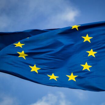 A close-up of the European Union flag with golden stars against a blue sky