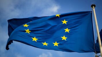 A close-up of the European Union flag with golden stars against a blue sky