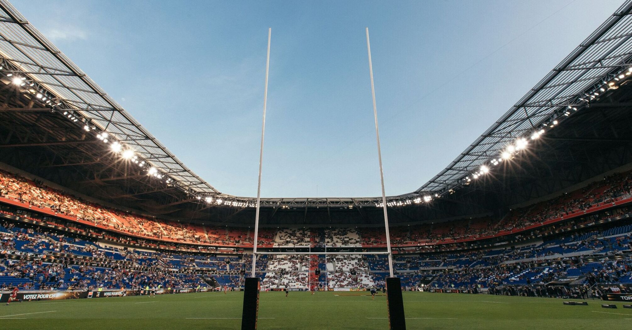 Rugby stadium with goalposts and a partially filled crowd during daylight