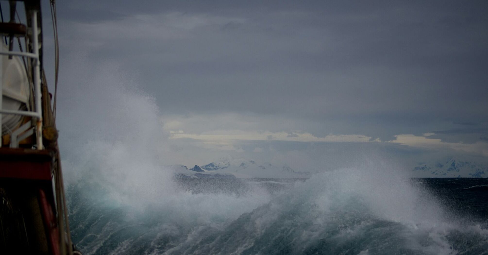 Stormy ocean waves crashing against a vessel under dark, overcast skies