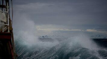 Stormy ocean waves crashing against a vessel under dark, overcast skies