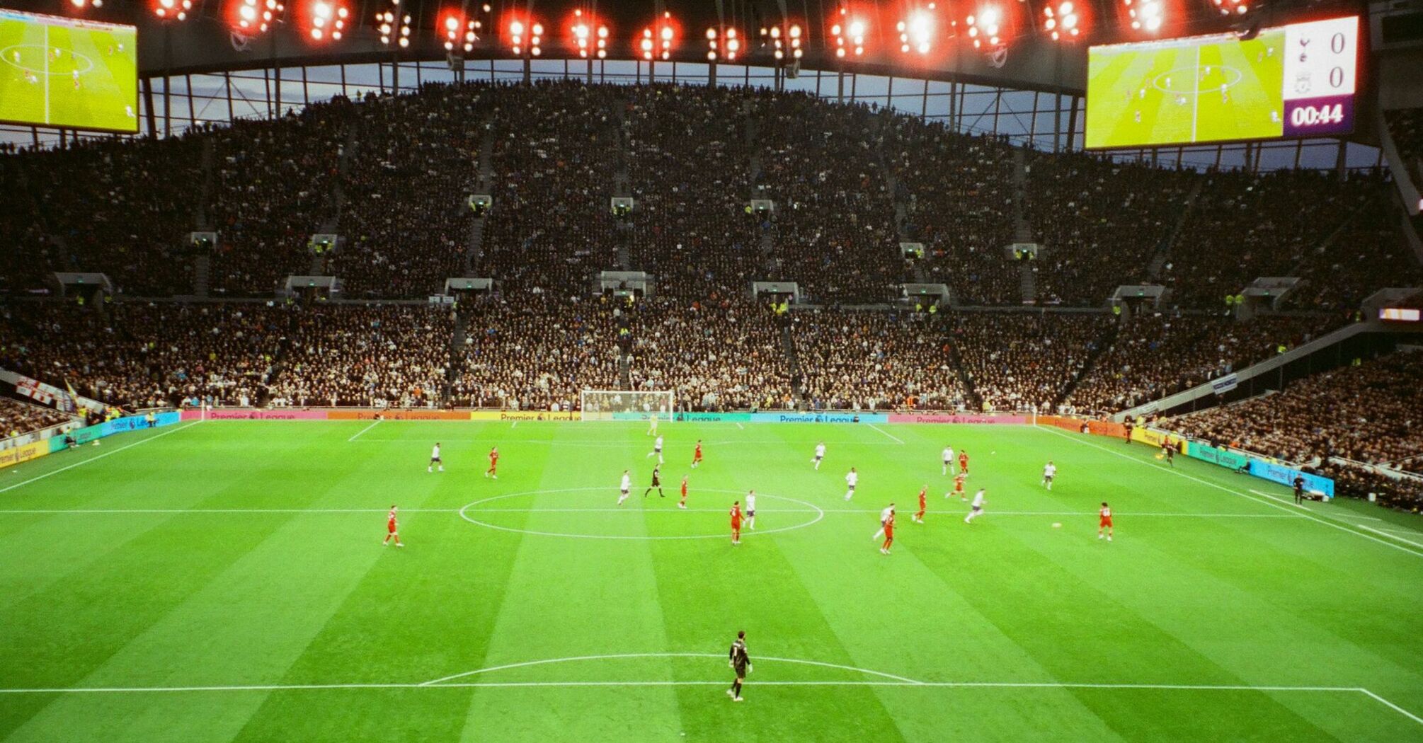 A packed football stadium during a match, featuring teams in white and red kits under bright stadium lights